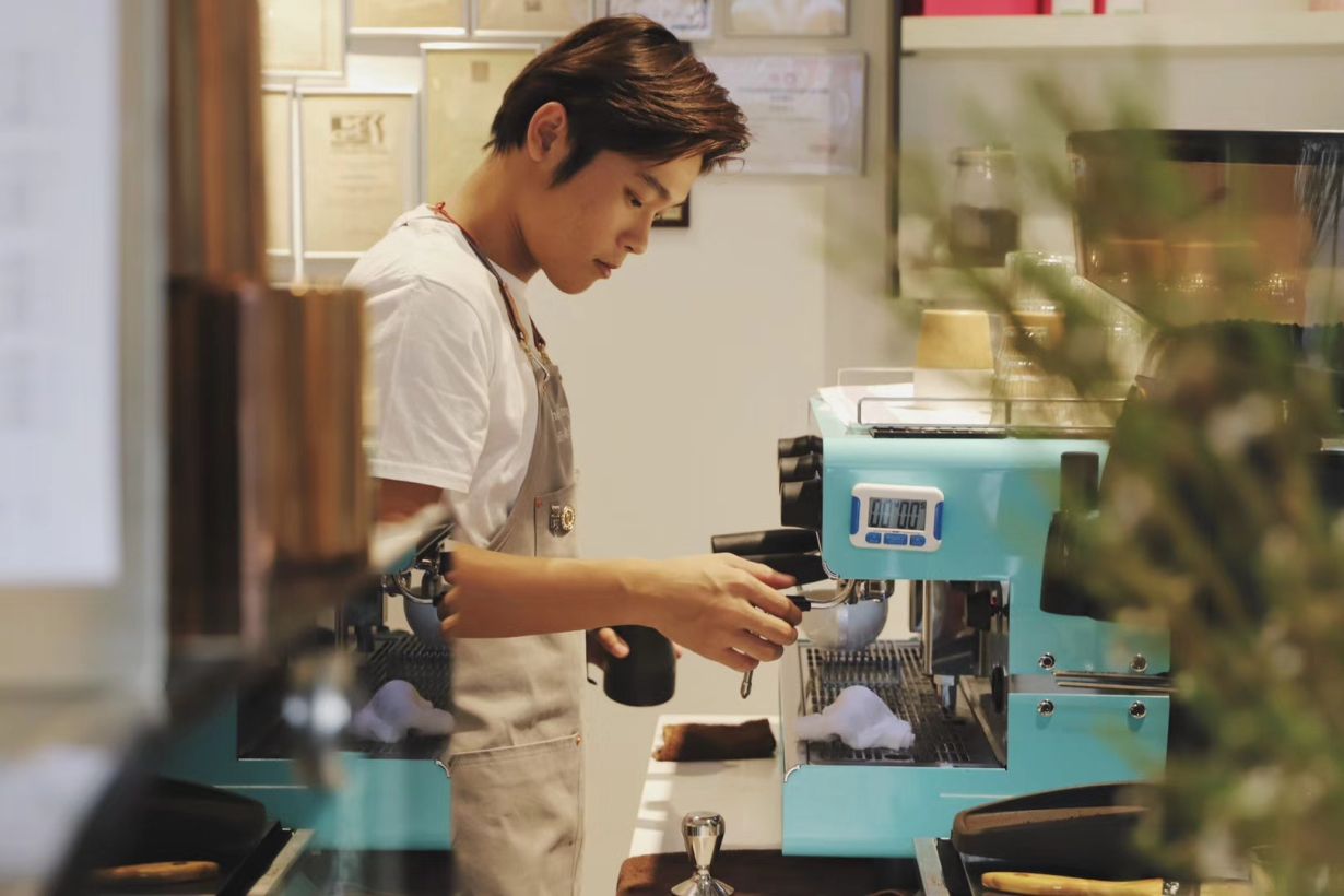 Barista profesional preparando café con una máquina espresso Iberital IB7 en color azul celeste en una cafetería moderna.